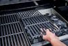 En hand lyfter ett grillgaller över grillkol i en utomhusgrill.