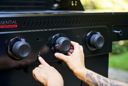 En hand vrider på en av fyra vred på en svart grill med texten "ESSENTIAL TRUE-INFRARED".