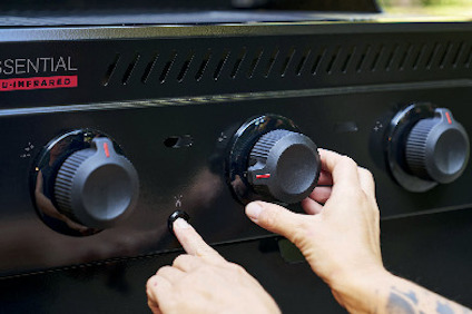 En hand vrider på en av flera svarta vred på en grill, bredvid texten "ESSENTIAL DUAL INFRAR RED".