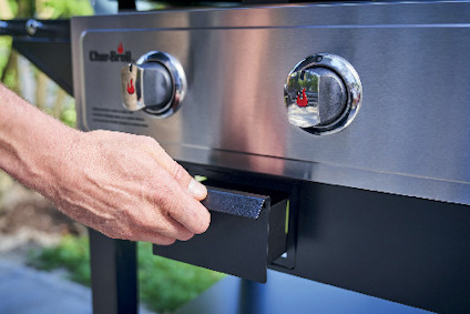 Hand drar i en låda under en rostfri grill med två vred, varav ett visar logotypen "Char-Broil".