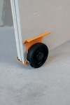 Orange vagnhjul fäst på ett skivmaterial, stående på ett betonggolv.