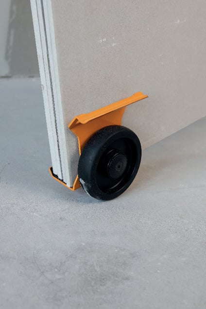 Orange vagnhjul fäst på ett skivmaterial, stående på ett betonggolv.