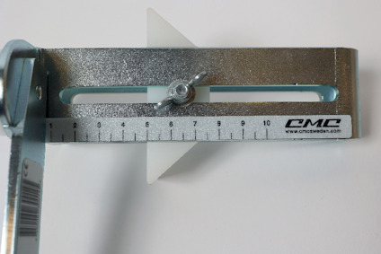 Metallregel med mätskala och justerbar plastindikator, märkt "CMC".
