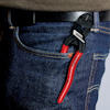 Tång med röda och svarta handtag fästad vid jeansficka med svart bälte ovanför.