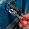 En hand använder en röd och grå Knipex tång för att greppa en bult på en blå metalldel.