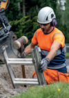 En person i skyddsutrustning använder en slägga för att slå på en metallstege vid en byggarbetsplats.