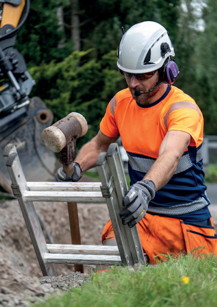 En person i skyddsutrustning använder en slägga för att slå på en metallstege vid en byggarbetsplats.