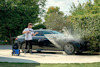 En person tvättar en svart bil med en högtryckstvätt på en solig dag.