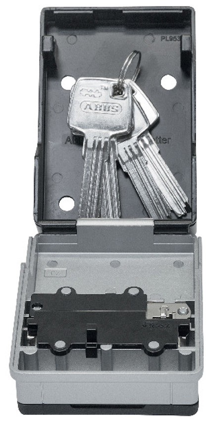 Grå nyckelbox med öppet lock och tre nycklar inuti. Lockets insida är svart.
