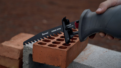 Sågblad, märkt "Starrett CARBIDE TIPPED", vilande på tegelsten och betongblock, hålls av en hand.