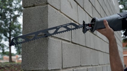 Person använder en tigersåg med lång sågklinga för att skära genom en vägg av betongblock.