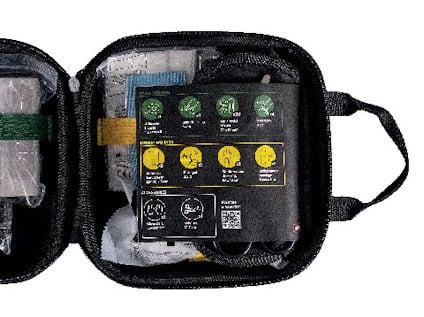 Öppen svart väska med medicinska förnödenheter, innehållande bandage, kompresser och instruktioner på locket.
