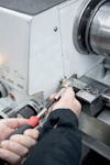 Händer justerar en metallmaskin med en skruvmejsel; skalan visar 30-4000 varv/min.