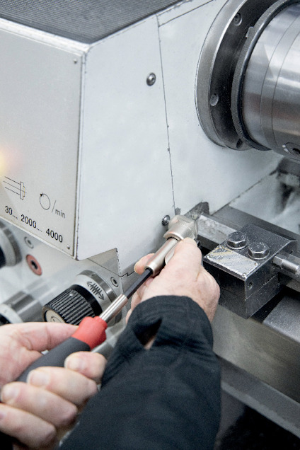 Händer justerar en metallmaskin med en skruvmejsel; skalan visar 30-4000 varv/min.