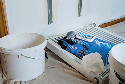 Vit hink och en påse med blått och svart tryck på ett element i ett rum under renovering.