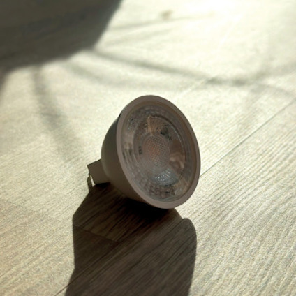 LED-lampa liggande på ett trägolv i solljus.