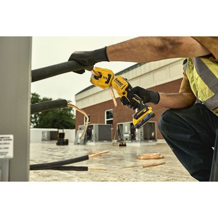 En person i arbetskläder använder en gul Dewalt-batteridriven verktygssåg på en byggarbetsplats.