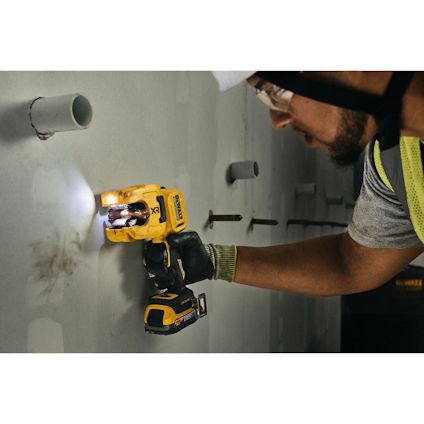 Person använder sladdlös borrmaskin med lampa mot en vägg; synliga rör och järnstänger.
