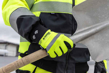 Person i reflexjacka och handskar håller en spade med trähandtag.
