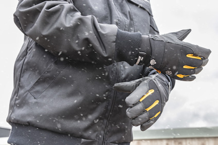 Person i vinterjacka och handskar står utomhus i snöfall.
